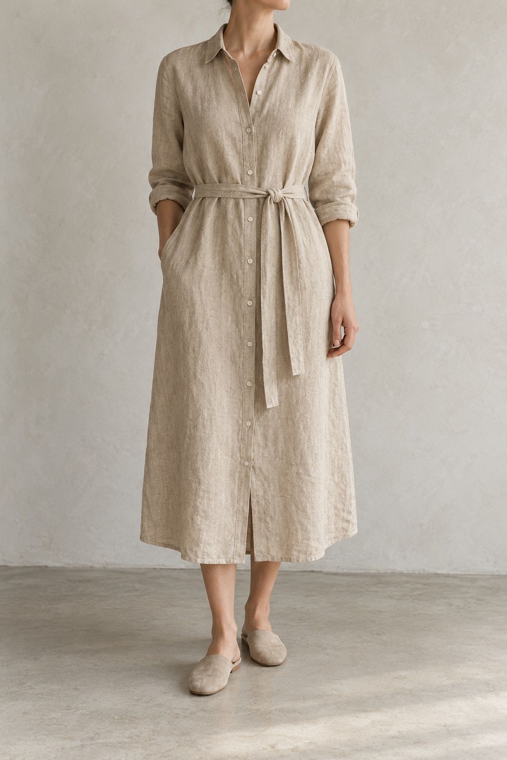 Maren shirt dress in flax with a loose tie belt, cropped at the chin against a pale plaster wall