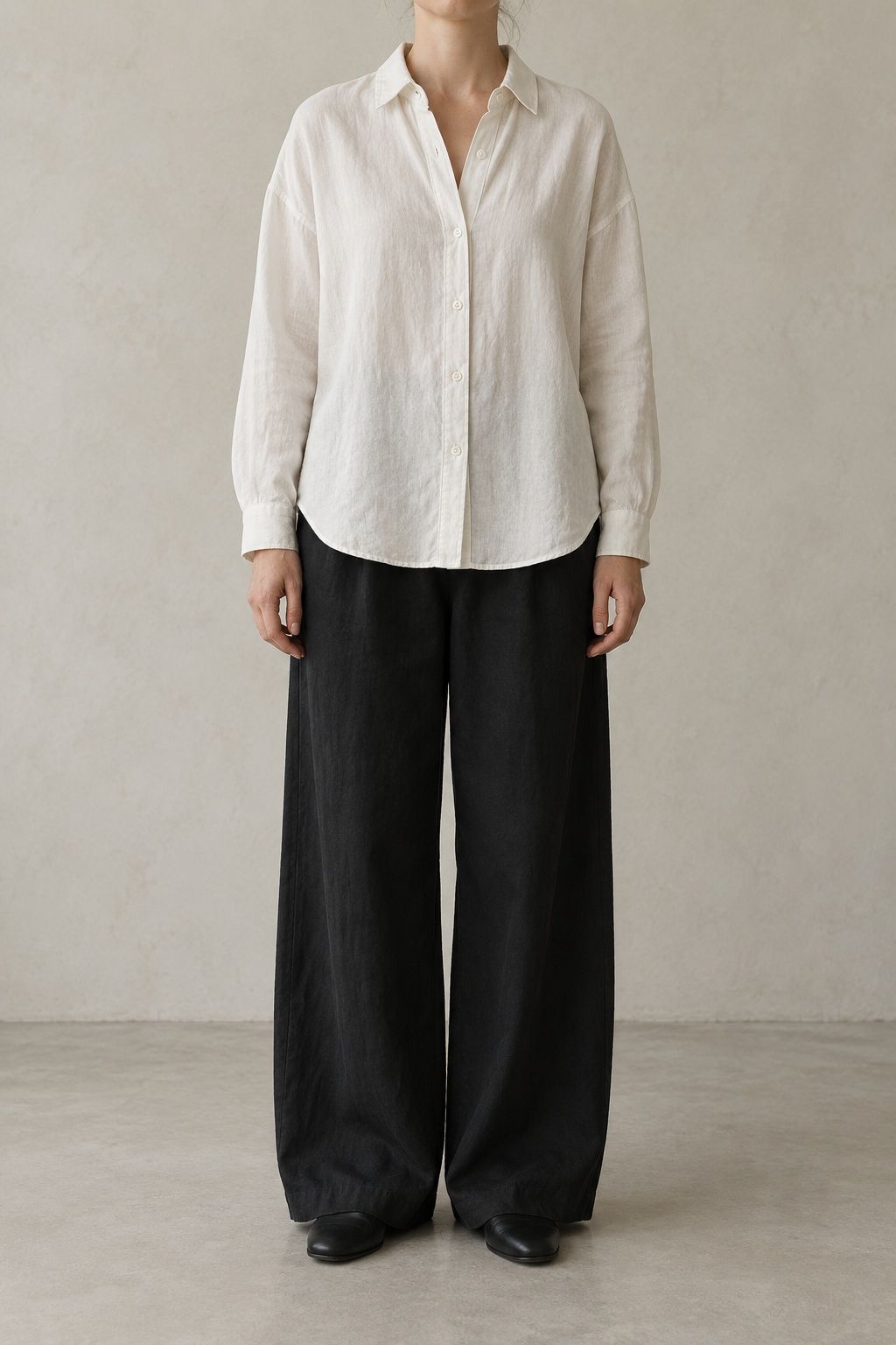 Orla linen shirt in chalk, worn loose and cropped at the chin, against a pale plaster wall