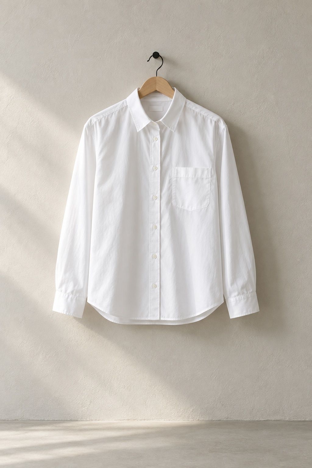 Tamsin poplin shirt in white on a plain wooden hanger against a pale plaster wall